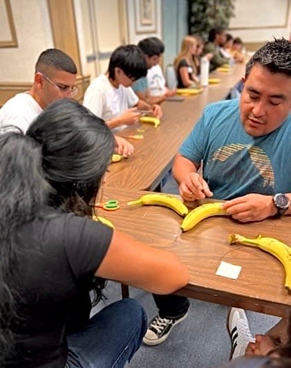 A group of people sitting around a table with bananas