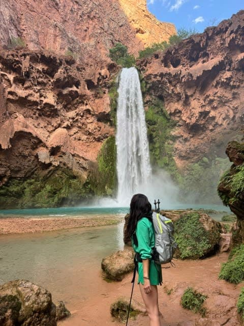 A woman with a backpack standing in front of a waterfall