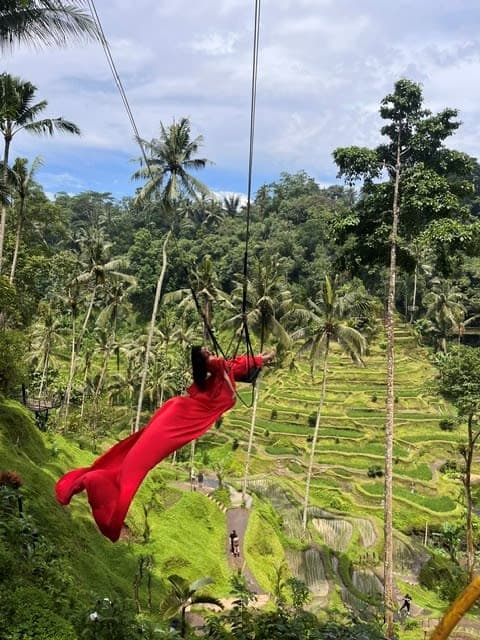 A woman in a red dress swinging from a rope