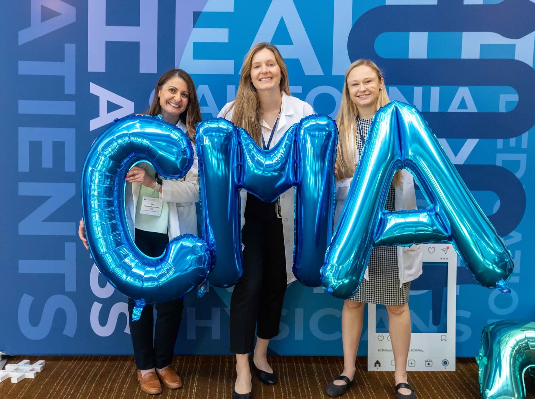 Three women standing in front of a blue wall holding up large letters